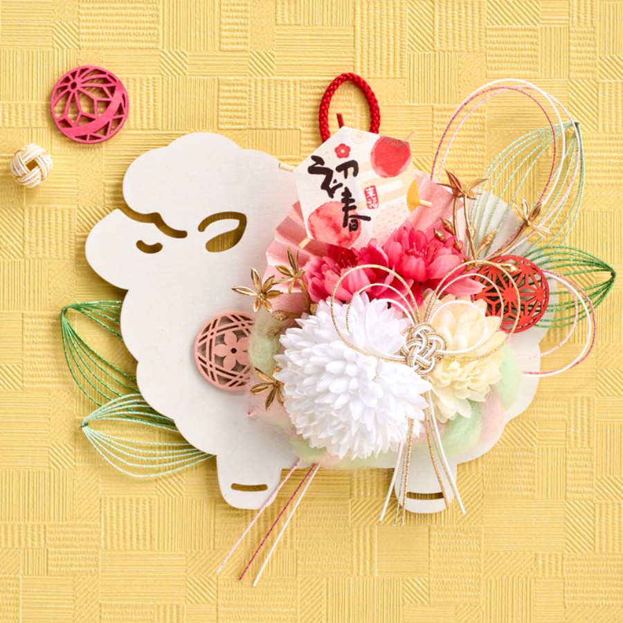 ひつじプレートお正月飾り 花材はグルーで接着しています。
いろいろな水引を使用し華やかに仕上げました。
羊のもこもこ感を意識してピンポンマムやカラーシープヘアを取り入れています。

作品サイズ(cm)：W20×D6×H21

 株式会社東京堂