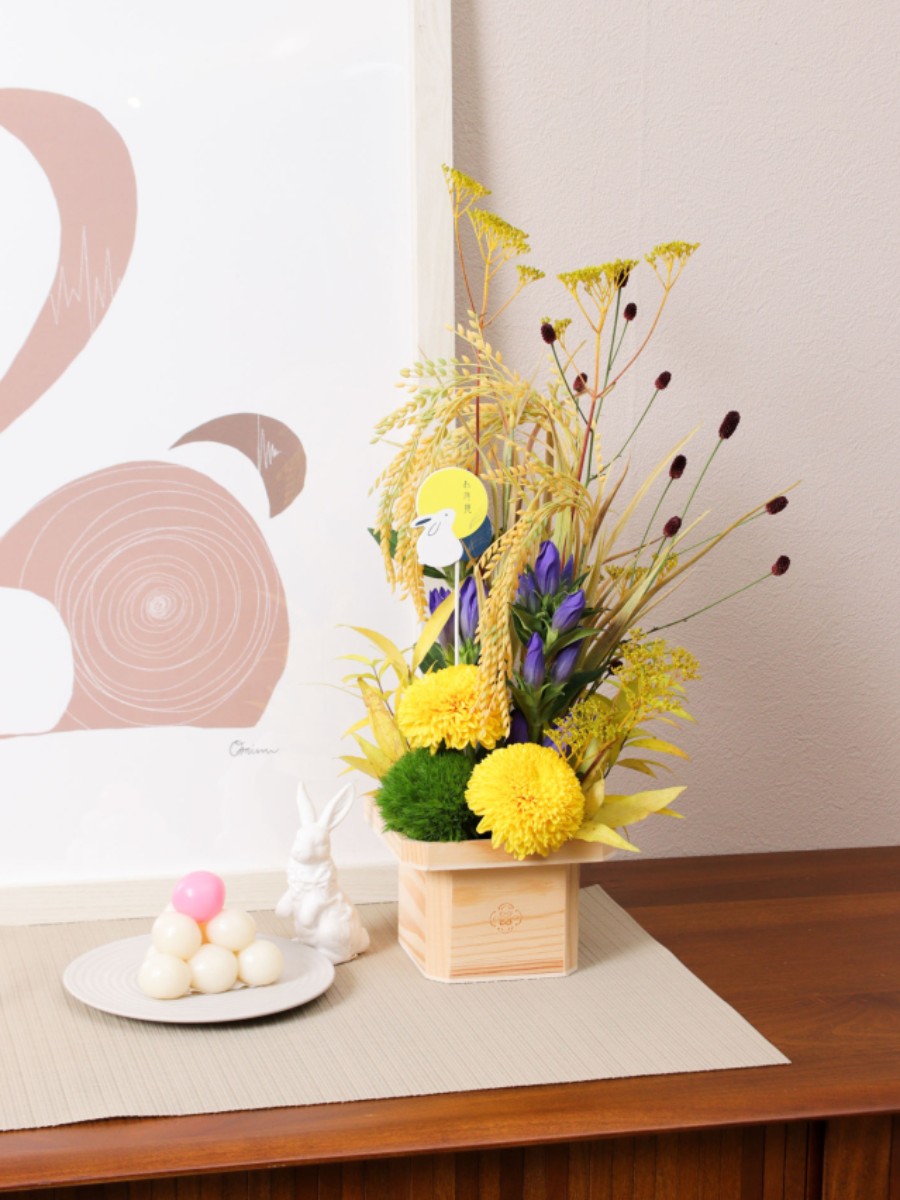 生花と造花のハイブリッドデザイン　お月見アレンジ お月見の代表的な花材であるススキは、豊穣祈願の象徴である稲穂に似ていることから使われていました。
稲穂はお月見の時期にはまだ入手できない花材ですが、実り豊かな稲穂を再現したアーティフィシャルフラワーで 横浜ディスプレイミュージアム